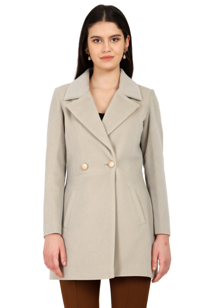 A woman is giving a standing side pose wearing Trufit’s double-breasted velvet coat in mint green with a lapel collar, side pockets, button closure, and brown tights.